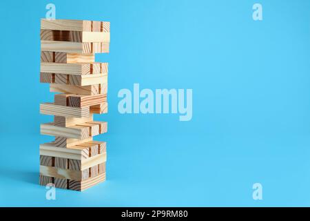 Jenga tower made of wooden blocks on light blue background, space for text Stock Photo