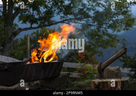 Metal brazier with burning firewood on backyard in mountains Stock Photo