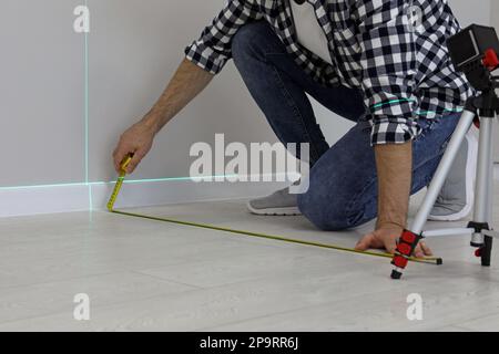 Man using cross line laser level and tape for accurate measurement on floor, closeup Stock Photo