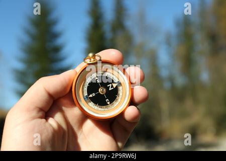 Man using compass for navigation during journey outdoors, closeup Stock Photo