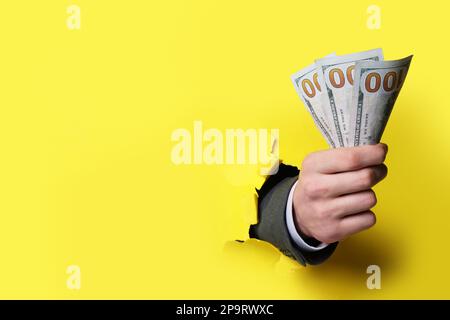 Businessman breaking through yellow paper with money in fist, closeup. Space for text Stock Photo