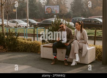 Two business colleagues talking about something while sitting on the bench at th park Stock Photo