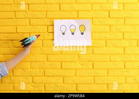 Woman holding toy rocket near yellow brick wall with lamps drawing, closeup. Startup concept Stock Photo