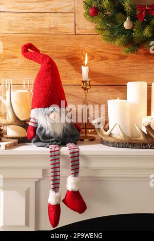 Cute Christmas gnome and festive decorations on mantelpiece in room Stock Photo