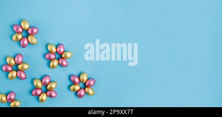 Flower shaped pile of Easter candy eggs wrapped in pink and golden foil on blue background. Happy Easter, springtime concept. Preparation for holiday. Stock Photo