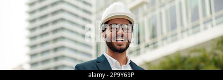 Indian construction architect in suit and hardhat making notes against modern building Stock Photo