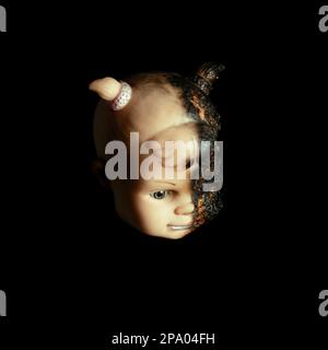 scary Isolated spooky possessed baby girl doll head creepy burnt face with gray eye on black background Close up macro Stock Photo