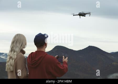 Young couple operating modern drone with remote control in mountains, back view Stock Photo