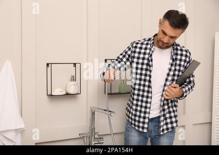 Plumber with clipboard checking water tap in bathroom Stock Photo