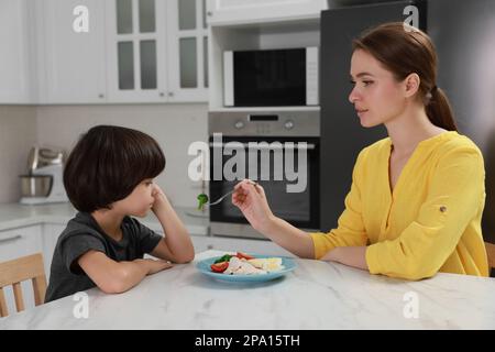 Mother feeding her son in kitchen. Little boy refusing to eat dinner Stock Photo