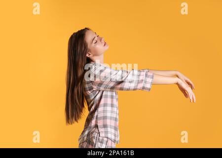 Young woman wearing pajamas in sleepwalking state on yellow background Stock Photo