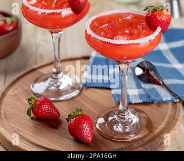 Strawberry margarita cocktail garnished with strawberries and salt rim on a wooden platter Stock Photo