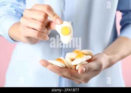 Woman holding handful of delicious gummy fried eggs shaped candies on pink background, closeup Stock Photo
