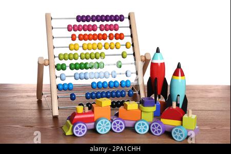 Bright toy train, abacus and rockets on wooden table against white background Stock Photo