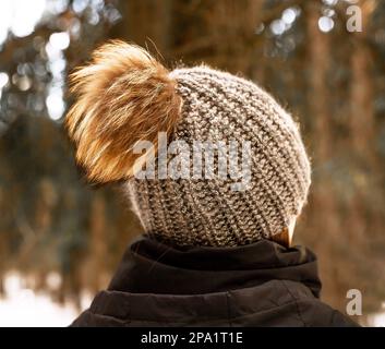 Knitted hat with fluffy pompom, back side view, on female head outdoors in winter nature. Stock Photo