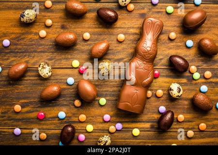 Chocolate Easter bunny with sweet chocolate eggs and colorful sweets on wooden background Stock Photo