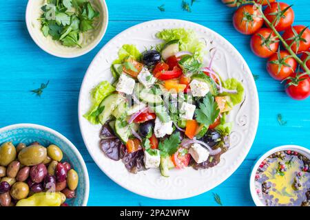 Greek salad bowl. Close-up. Bowl with fresh greek salad, tomatoes, olives, olive oil on wooden table. Healthy eating concept. Top view. Traditional Stock Photo