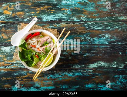 Traditional Vietnamese soup Pho bo with herbs, meat, rice noodles, broth. Pho bo in bowl with chopsticks, spoon. Space for text. Top view. Asian soup Stock Photo