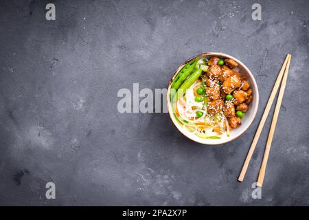 Asian style noodles with teriyaki chicken, vegetables and green peas pods. Noodles in bowl on rustic concrete background. Chinesethaijapanese style Stock Photo