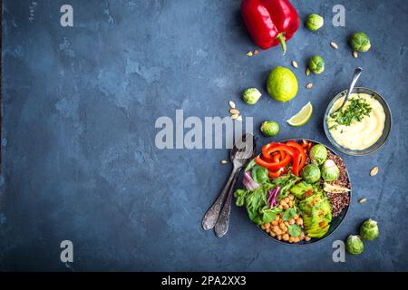 Bowl with healthy salad, dip, blue stone background. Top view. Space for text. Buddha bowl with chickpea, avocado, quinoa seeds, red bell pepper Stock Photo