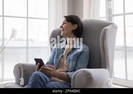 Happy thoughtful attractive mature woman thinking over online content Stock Photo