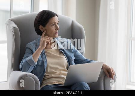 Thoughtful mature woman sitting in armchair at home Stock Photo