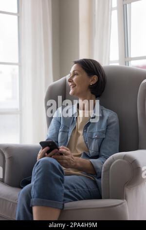 Cheerful positive middle aged woman thinking over text message Stock Photo