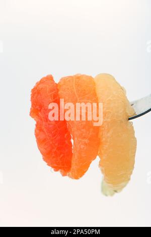 Different coloured grapefruit segments pierced on fork ready to eat against a white background. Stock Photo