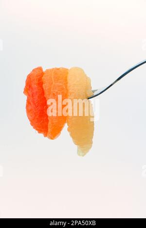 Different coloured grapefruit segments pierced on fork ready to eat against a white background. Stock Photo