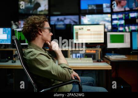 System administrator sitting in chair looking at computer screen in server room Stock Photo