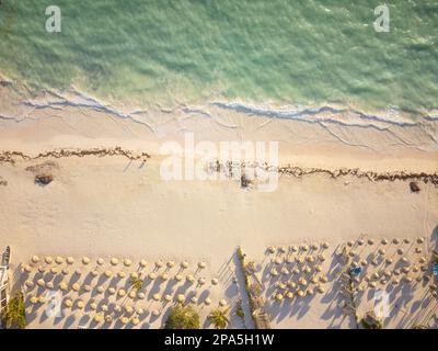 Shooting from a drone. Sea coast. Clear turquoise water with light white waves crashes onto a white sandy beach. There are many beach umbrellas in the Stock Photo