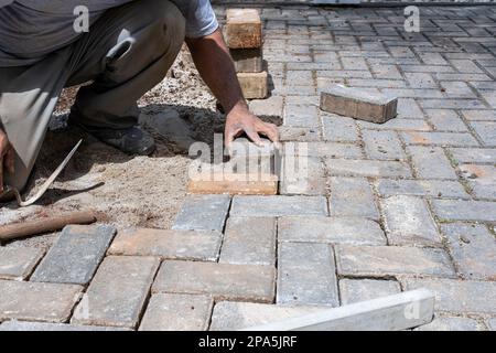 Brazilian construction worker placing and leveling concrete block on the ground. Stock Photo