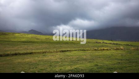 A breathtaking panorama of storm clouds looming over the lush green hills and grasslands of Asturias, creating a dramatic yet peaceful atmosphere. Stock Photo