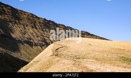 Walker ascending the path to Llyn y Fan Fawr beneath the Old Red Sandstone cliffs of Fan Hir in the Brecon Beacons National Park of South Wales UK Stock Photo