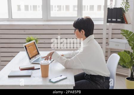 Portrait of beautiful middle aged brunette businesswoman sitting at light modern work place office and typing on laptop Stock Photo