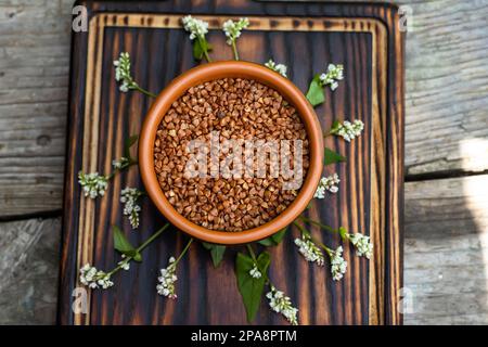 Dry buckwheat in a clay brown plate. Top view of a cutting wooden board with organic dry grits Fagopyrum esculentum Stock Photo