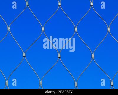 stainless steel twisted wire cable fence closeup. diamond pattern shape net. clear blue sky background. modern silver color fence material. macro view Stock Photo