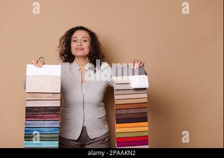 Charming woman, interior designer, decorator showing you fabric samples for sofa upholstery, isolated beige background Stock Photo
