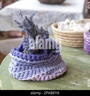 Square format, and the main focus of the image is lavender plant in a blue crochet flowerpot. The pot is handmade and has a delicate, textured look to Stock Photo