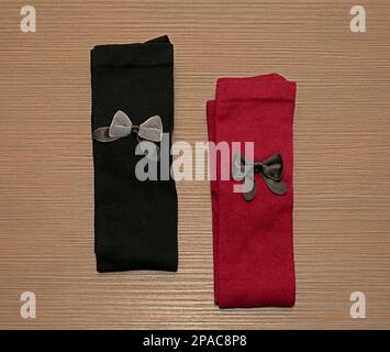 Black and red cotton material socks with decorative bows folded on wooden table surface Stock Photo