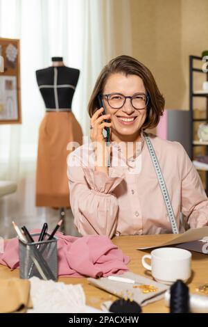 Woman clothes fashion designer talking on the phone with a client in the studio. Businesswoman seamstress. Stock Photo