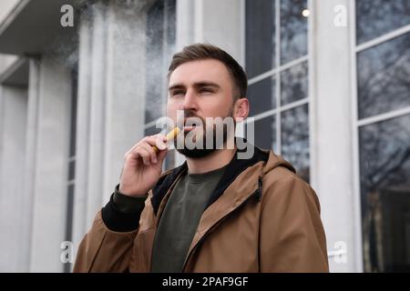 Handsome young man using disposable electronic cigarette outdoors Stock Photo