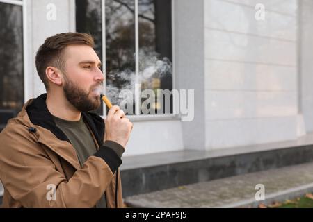 Handsome young man using disposable electronic cigarette outdoors Stock Photo