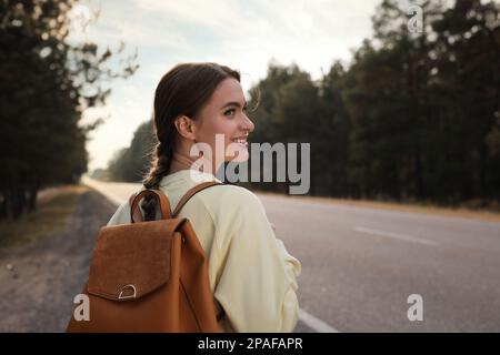 Young woman with backpack on road near forest Stock Photo