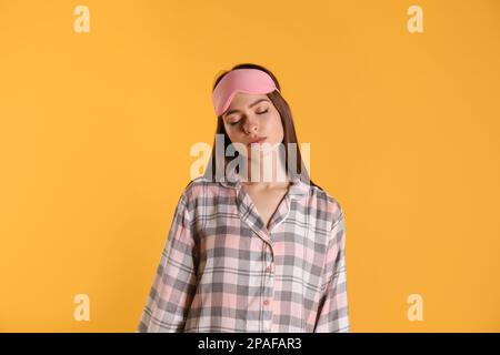 Young woman wearing pajamas and mask in sleepwalking state on yellow background Stock Photo