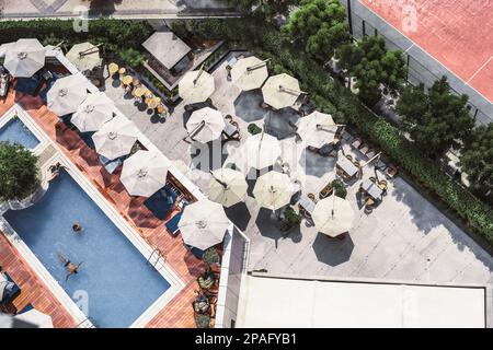 Shot from a drone, an outdoor bar with multiple open sunshades forms a nice landscape. Adjacent to the terrace lies a lush garden, while the other sid Stock Photo