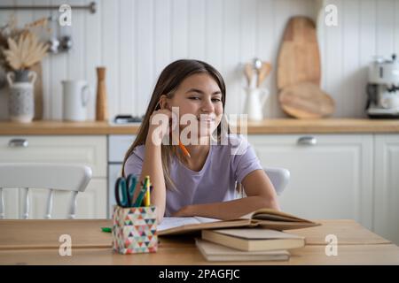 Portrait of happy child schoolgirl sitting at table with textbooks at home doing school homework Stock Photo