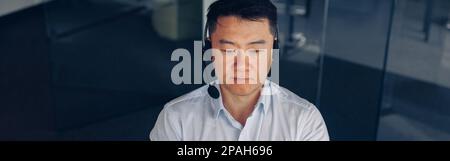 Asian businessman in headphones working on computer in modern coworking Stock Photo