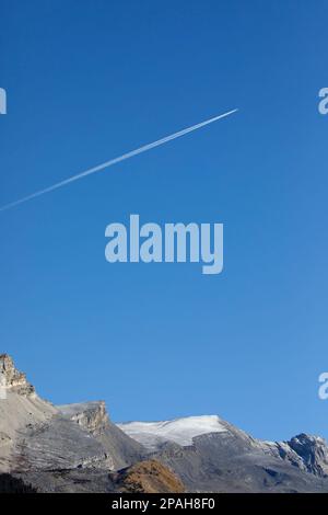 Airplane with contrails in blue sky over the Rocky Mountains, Jasper National Park, Canada Stock Photo