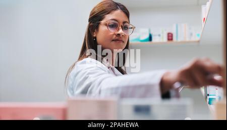 Female drug store worker getting medication from a shelf. Pharmacist filling a prescription in a chemist. Female healthcare worker in a pharmacy. Stock Photo